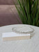 Teter Warm Rhinelline silver floral headpiece displayed on a textured surface with green plants in background.