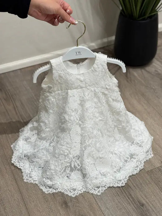Teter Warm Rosalyn off-white floral lace baptism dress displayed on a hanger on wood floor.