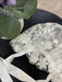 Teter Warm scalloped edge baby bonnet with floral lace, displayed on a black surface near a plant.