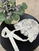 Teter Warm scalloped edge baby bonnet with floral lace detail displayed on a black table beside a potted plant.