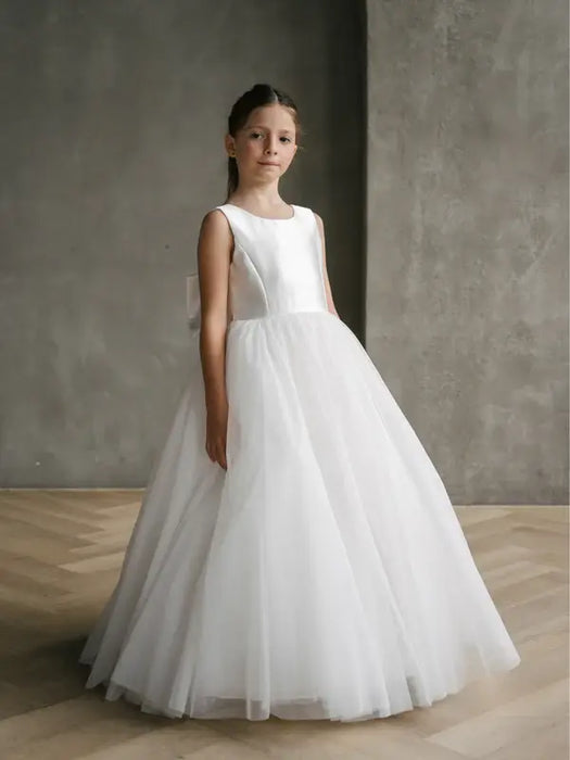 Teter Warm Shelly Satin Bow Communion Dress shown on a young girl standing indoors against a gray wall.