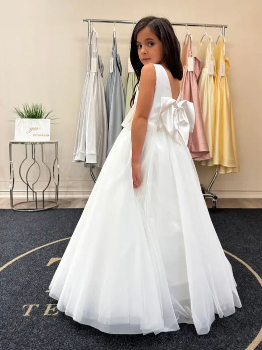 Teter Warm Shelly Satin Bow Communion Dress on a girl standing in a boutique with pastel dresses in the background.