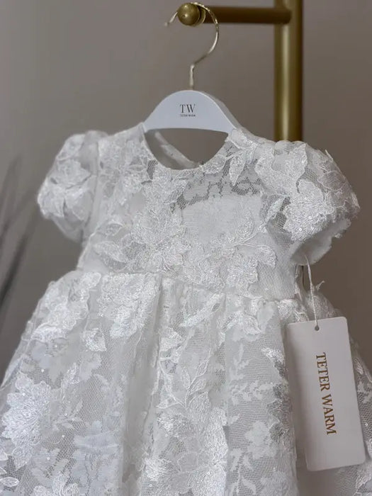 Teter Warm Sia off-white floral lace baptism dress hanging on a hanger with tag visible.