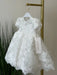 Teter Warm off-white floral lace baptism dress with puff sleeves shown hanging on a rack.