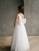 Sylvia Satin Pearl Communion Dress shown on a young girl with a large back bow, standing indoors.