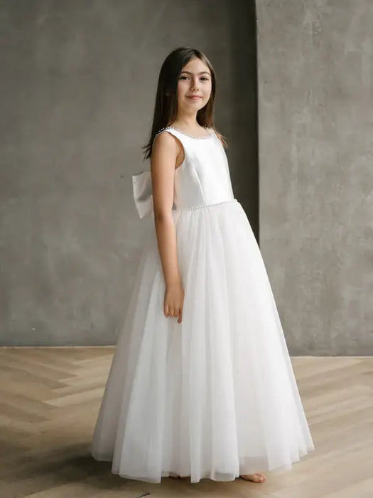 Sylvia Satin Pearl Communion Dress shown on a young girl standing indoors on wood floor
