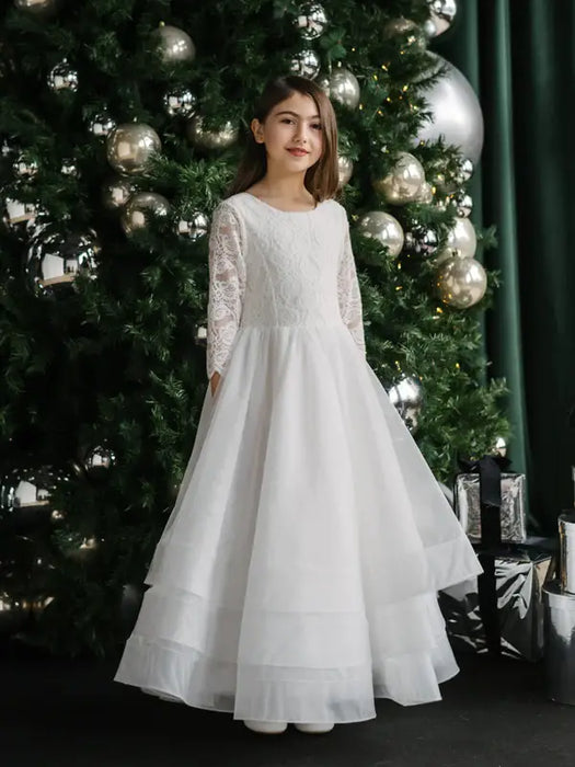 Teter Warm Taula Lace Communion Dress with long lace sleeves worn by a girl standing by a decorated Christmas tree.