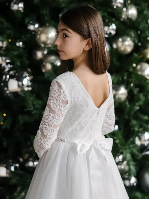 Teter Warm Taula lace communion dress with long sleeves, shown on a girl standing by a Christmas tree.