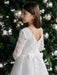 Teter Warm Taula lace communion dress with long sleeves, shown on a girl standing by a Christmas tree.