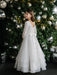 Teter Warm Taula Lace Communion Dress shown on a girl standing in front of a decorated Christmas tree.
