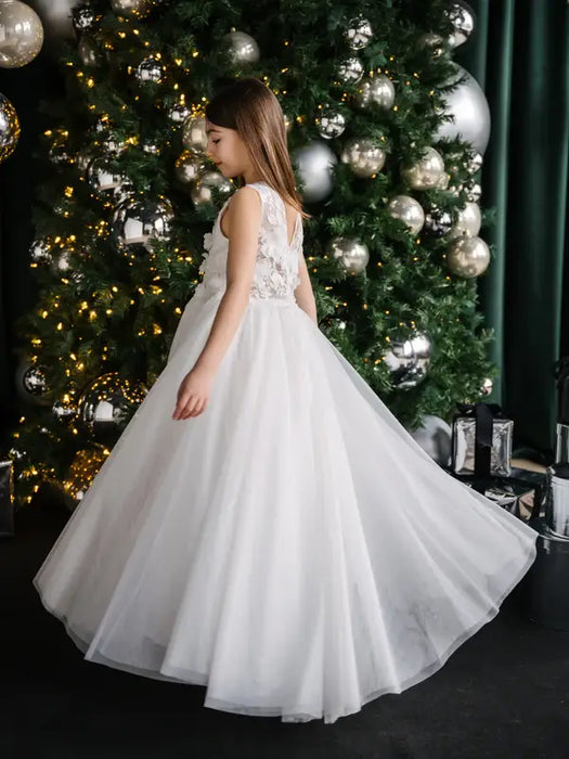 Teter Warm Thea off-white communion dress shown on a girl standing by a decorated Christmas tree.
