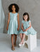 Teter Warm Tiffany Blue sleeveless party dresses on two young girls in a studio setting.