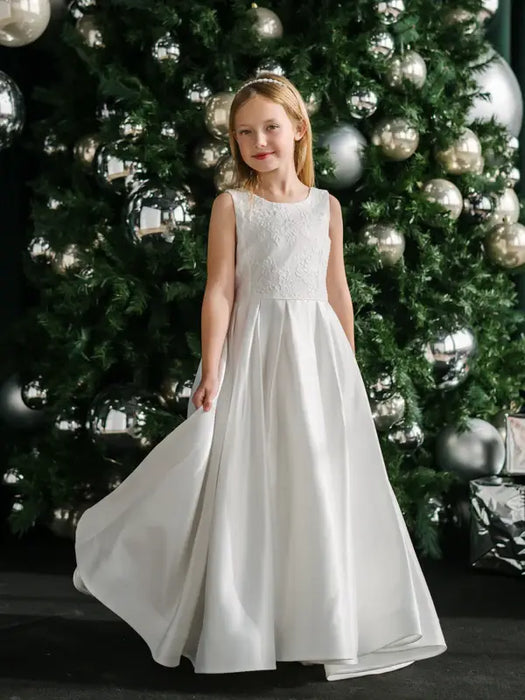 Teter Warm Tori off-white lace communion dress worn by girl standing in front of decorated Christmas tree.