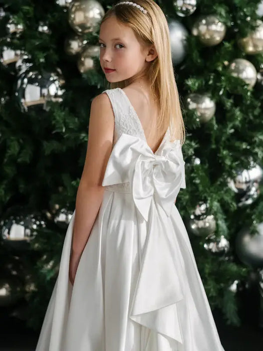 Teter Warm Tori off-white lace communion dress with large back bow, worn by girl in front of decorated tree.