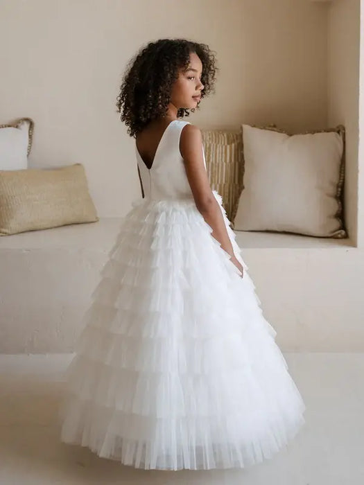Teter Warm Winniw off white communion dress shown on a young girl standing indoors by cushions.