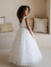 Teter Warm Winniw off white communion dress shown on a young girl standing indoors by cushions.