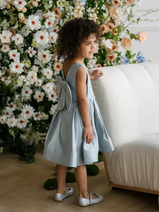 Teter Warm Zelda Blue Party Dress worn by a child standing near a white sofa and floral backdrop.