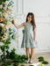 Teter Warm Zelda Blue Party Dress worn by a young girl standing by floral decorations indoors.