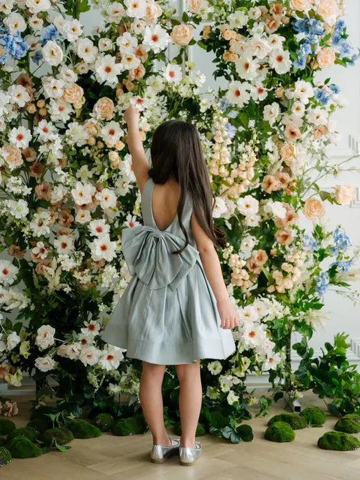 Teter Warm Zelda Blue Party Dress worn by a girl standing in front of a floral backdrop.