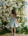 Teter Warm Zelda Blue Party Dress worn by a girl standing in front of a floral backdrop.