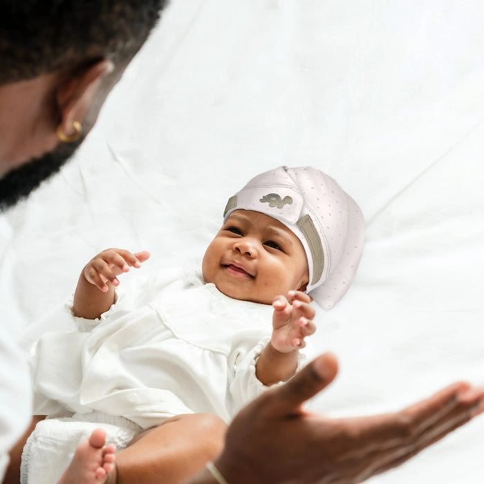 Smiling baby in Tortle Air Turtle Trot beanie on bedding