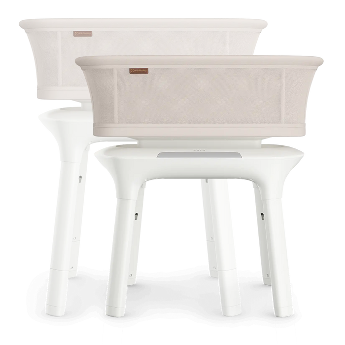 Modern beige baby bassinet with mesh sides and white legs, shown in duplicate on white background.