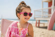 Uveez neon pink sunglasses worn by a smiling child at the beach, holding a pink towel.