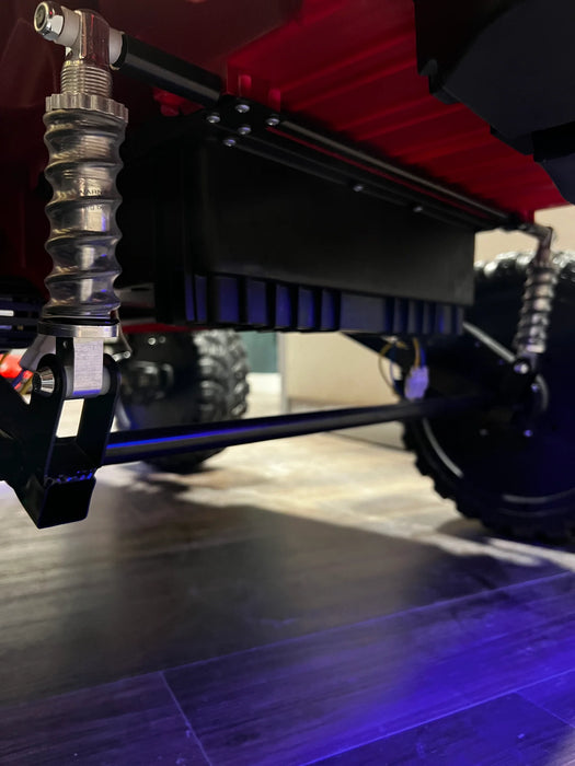 Voltz Toys F-450 lifted ride-on car undercarriage close-up showing suspension and wheels indoors.